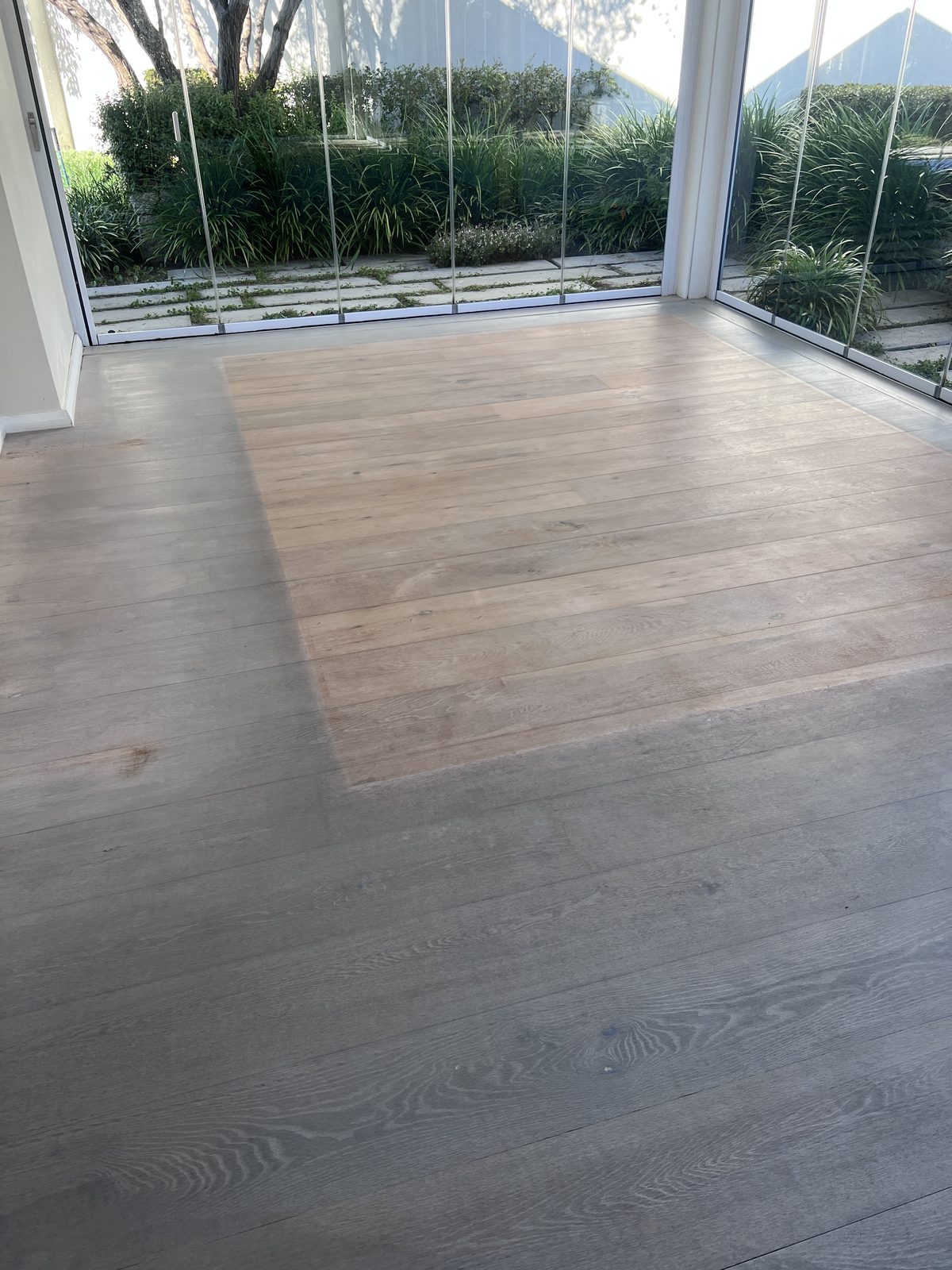 Worn oak floor before sanding, showing patchy discolouration by the glass doors
